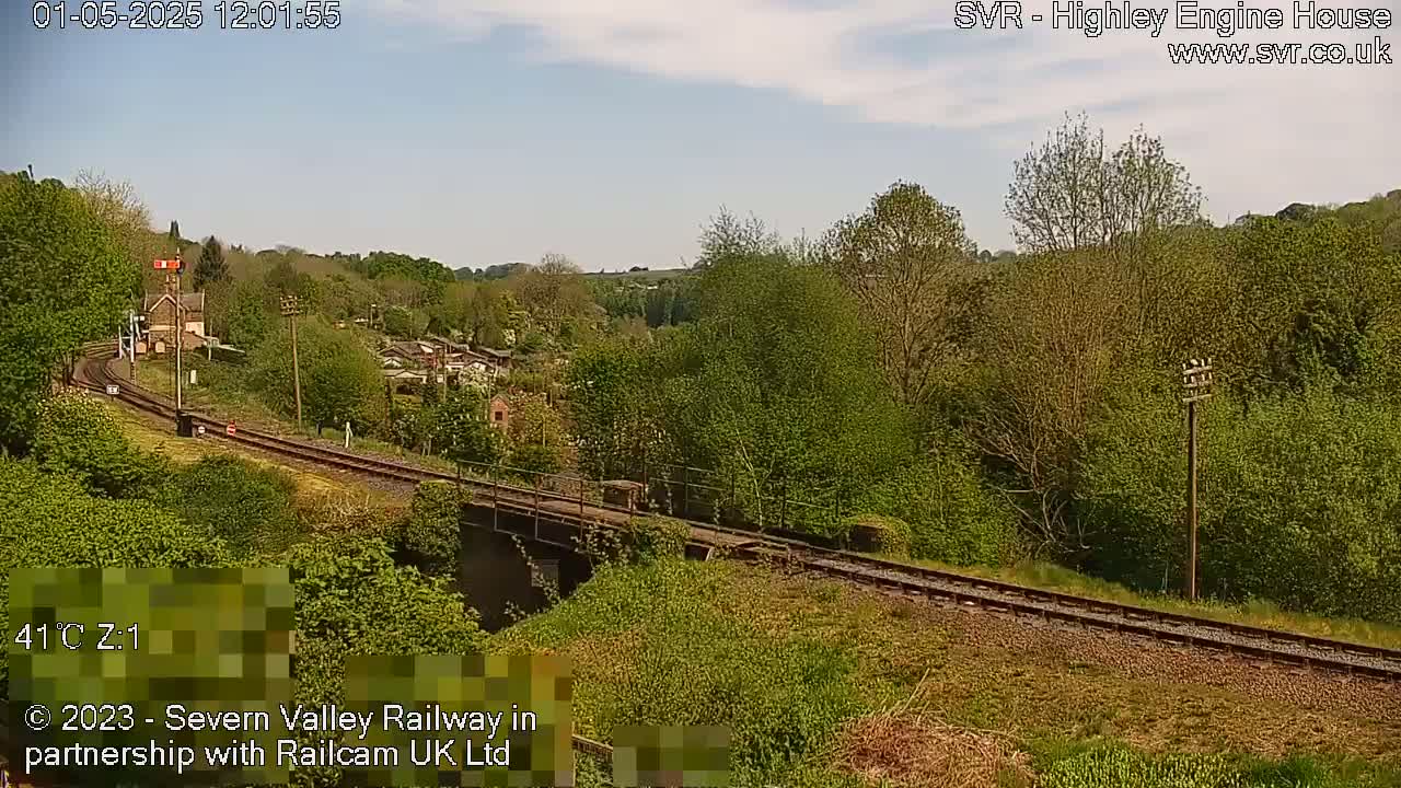 A railway line curves through a lush green landscape under a partly sunny sky.