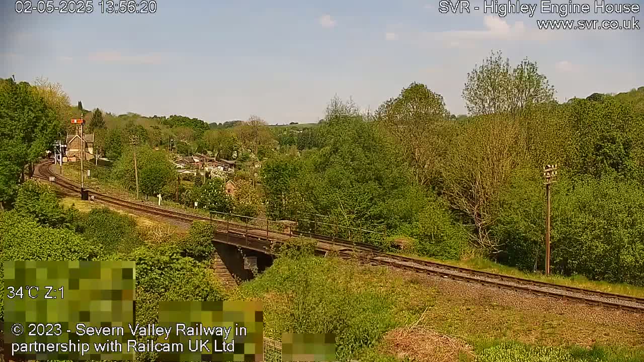 A railway line curves through a lush green valley on a sunny day.