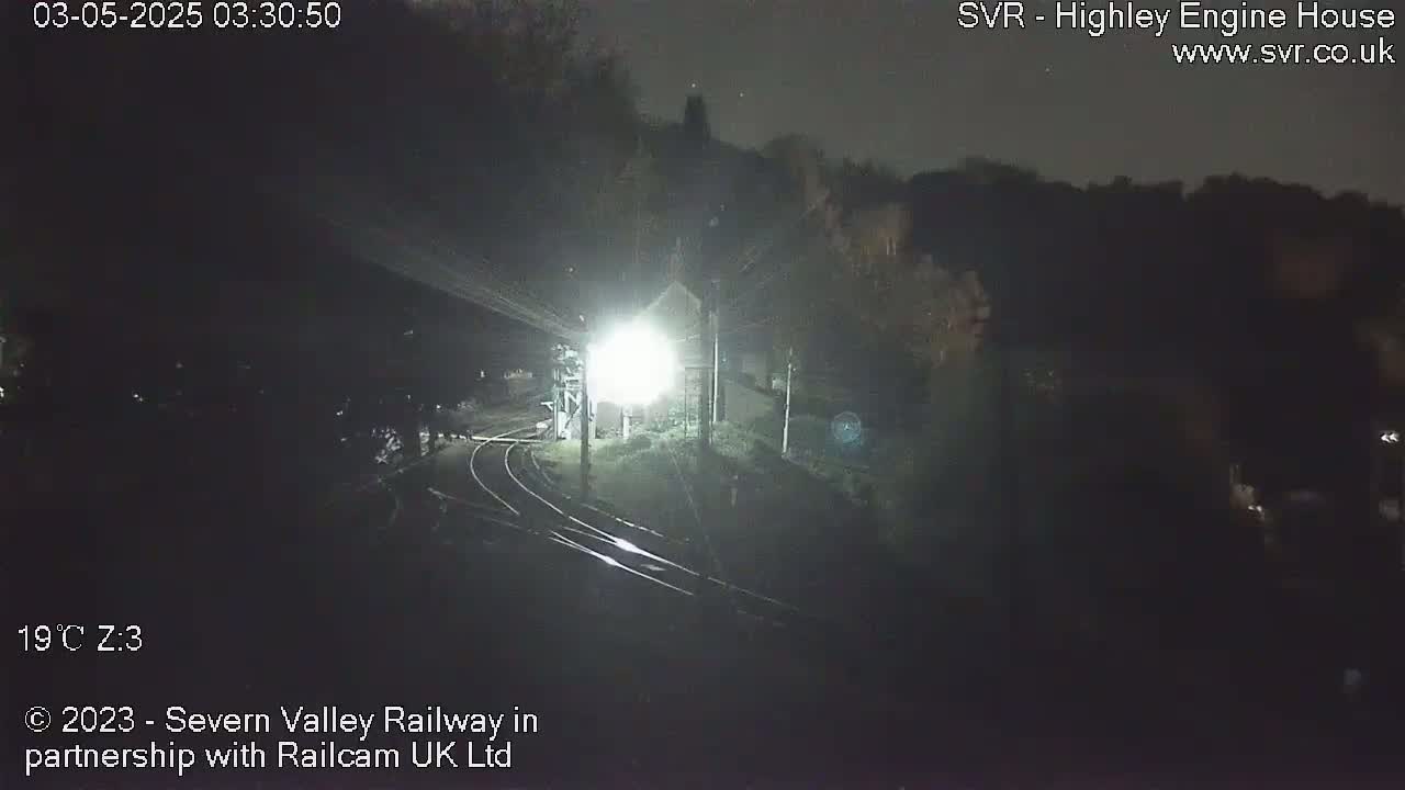 A nighttime, dimly lit view of train tracks and a building, possibly a train station, under a dark sky.