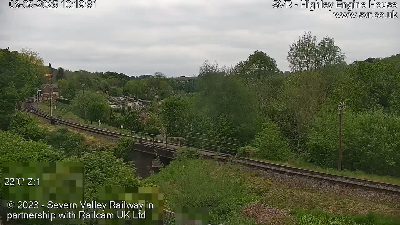 A train track curves through a lush green landscape under an overcast sky.