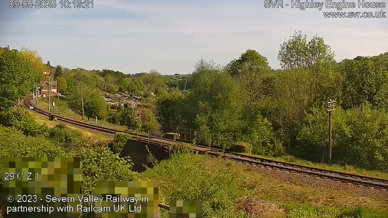 A railway line curves through a lush green landscape under a mostly clear sky.