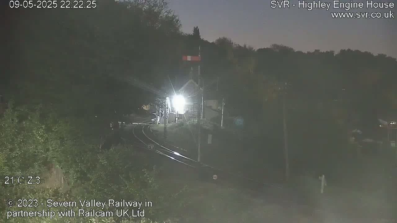 A nighttime view of a train station with train tracks and a bright light illuminating the area.