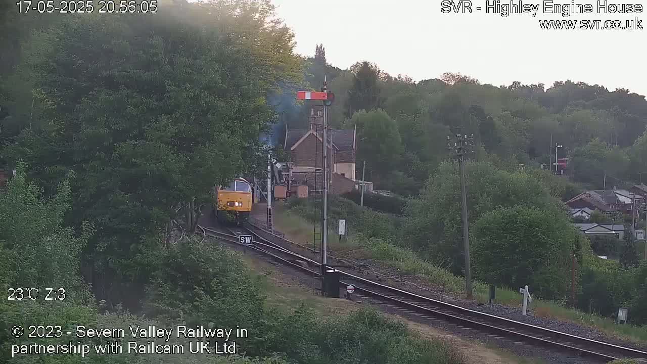 A yellow diesel locomotive is approaching a railway station on a partly cloudy evening.
