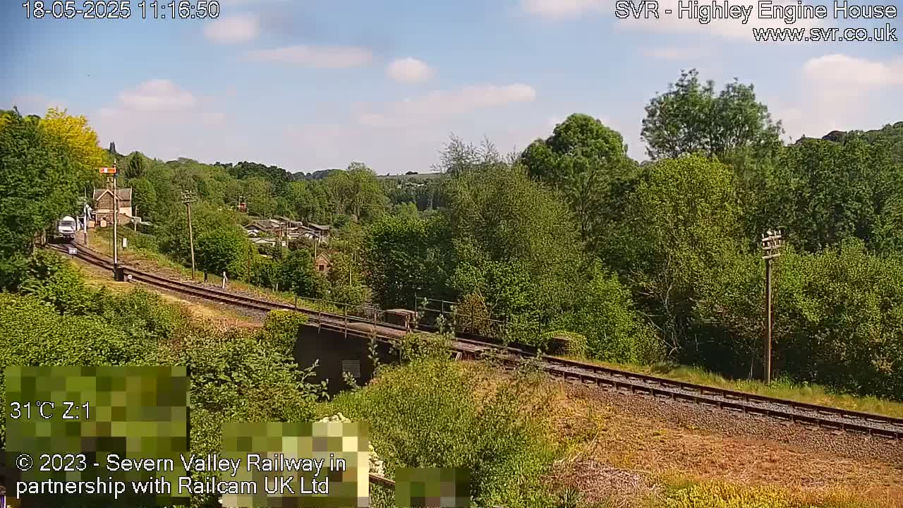A train is traveling along a railway track that curves through a lush green landscape on a sunny day.