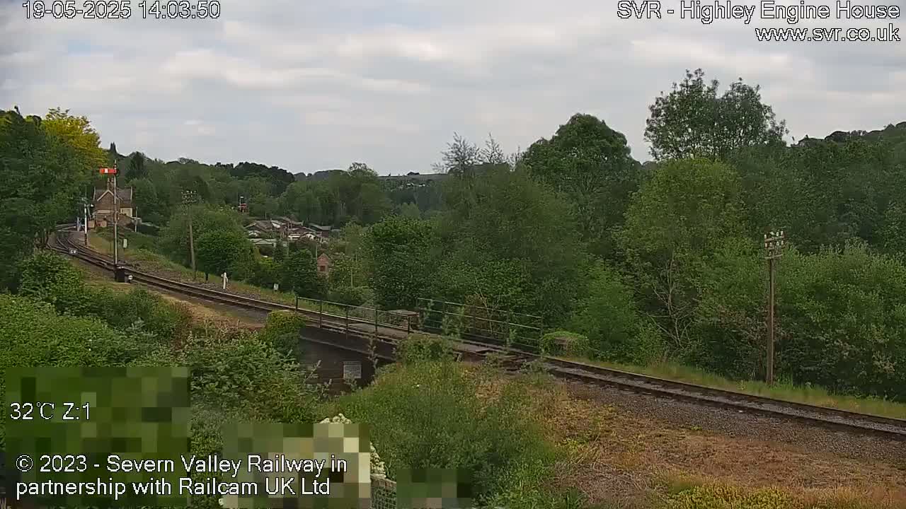 A railway line curves through a lush green landscape under a partly cloudy sky.