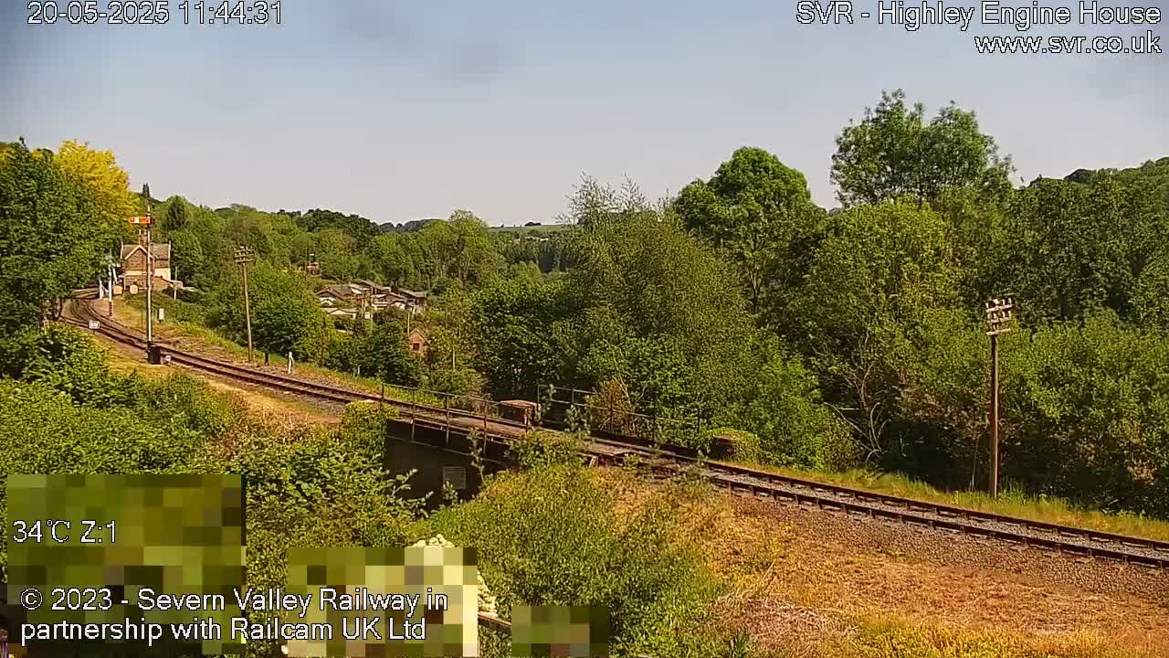 A sunny view of a railway track winding through a lush green landscape, passing over a bridge.
