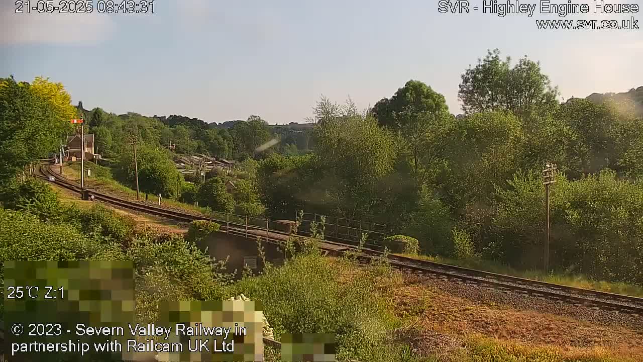 A sunny view of a railway track curving through a green, wooded landscape.