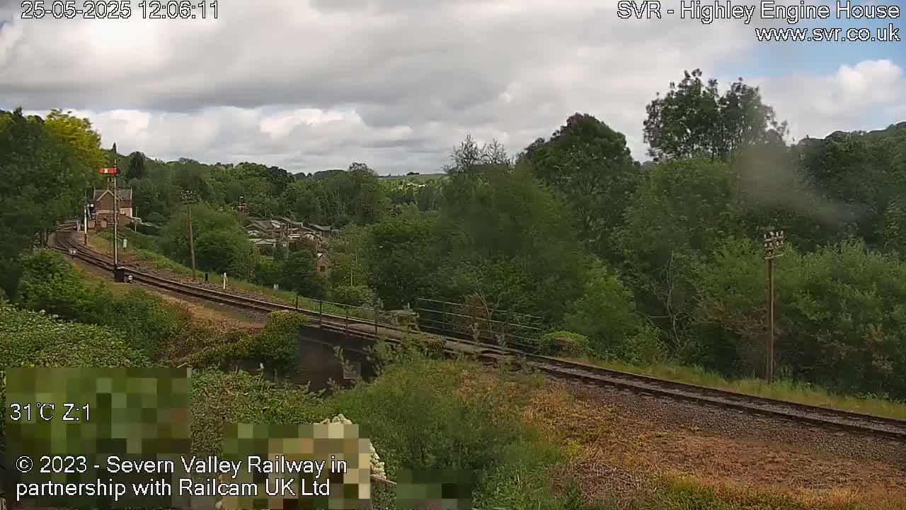 A train track curves through a lush green landscape under a partly cloudy sky.