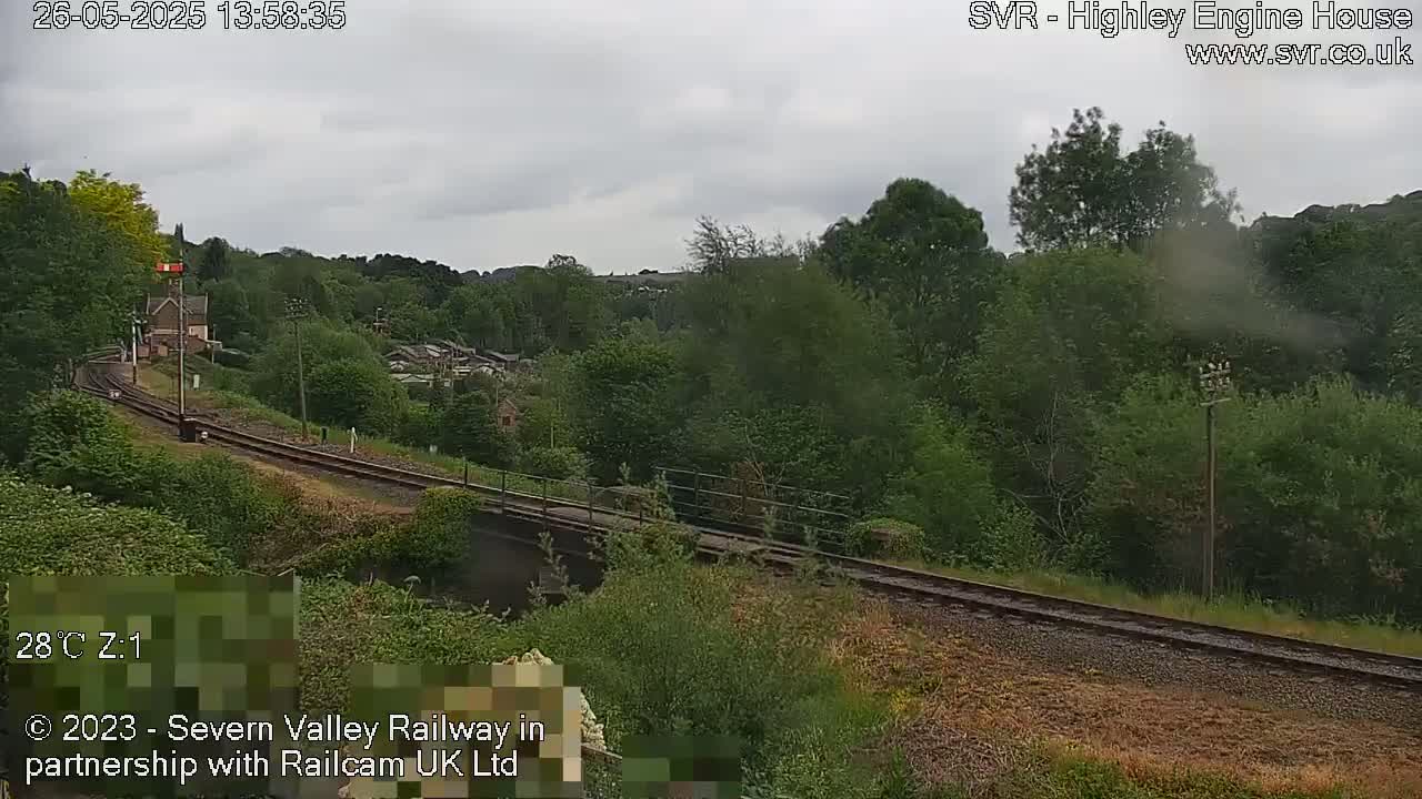 A railway track curves through a green, wooded valley under an overcast sky.