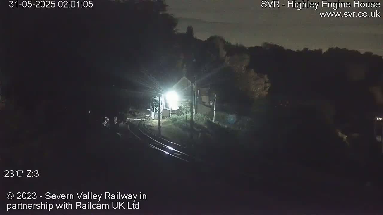 A nighttime, dimly lit view of train tracks near a building and trees under a dark sky.