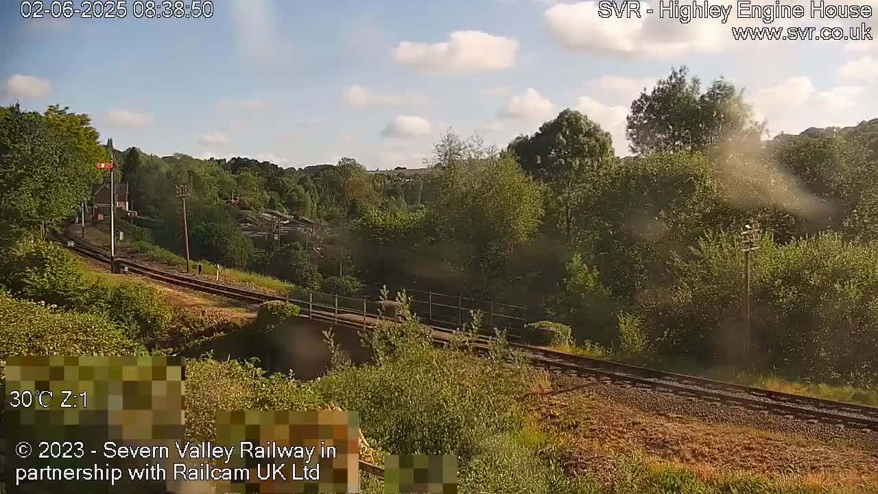 A sunny view of a railway track winding through a lush green landscape.