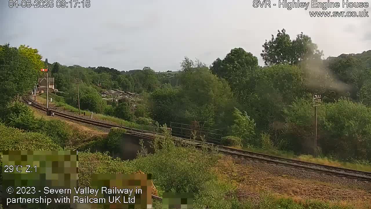 A railway track curves through a lush green landscape under a partly cloudy sky.