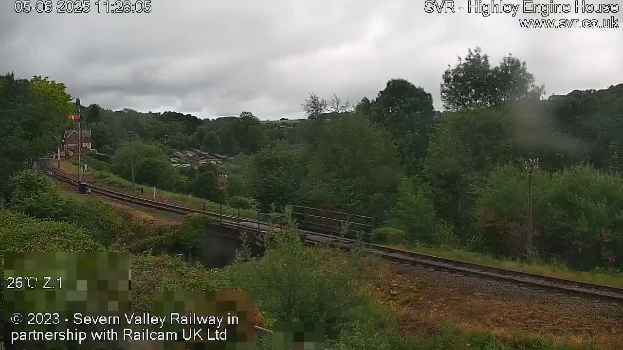 A railway line curves through a lush green landscape under an overcast sky.