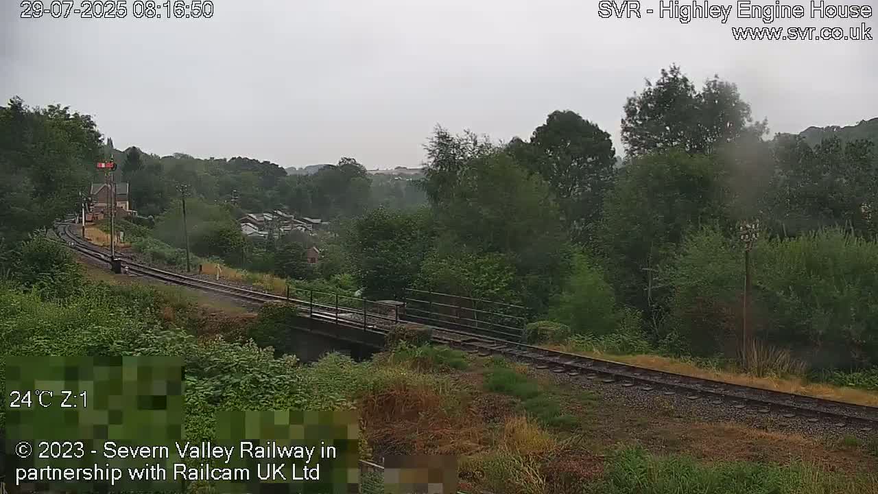 A railway track curves through a lush green landscape on an overcast day.