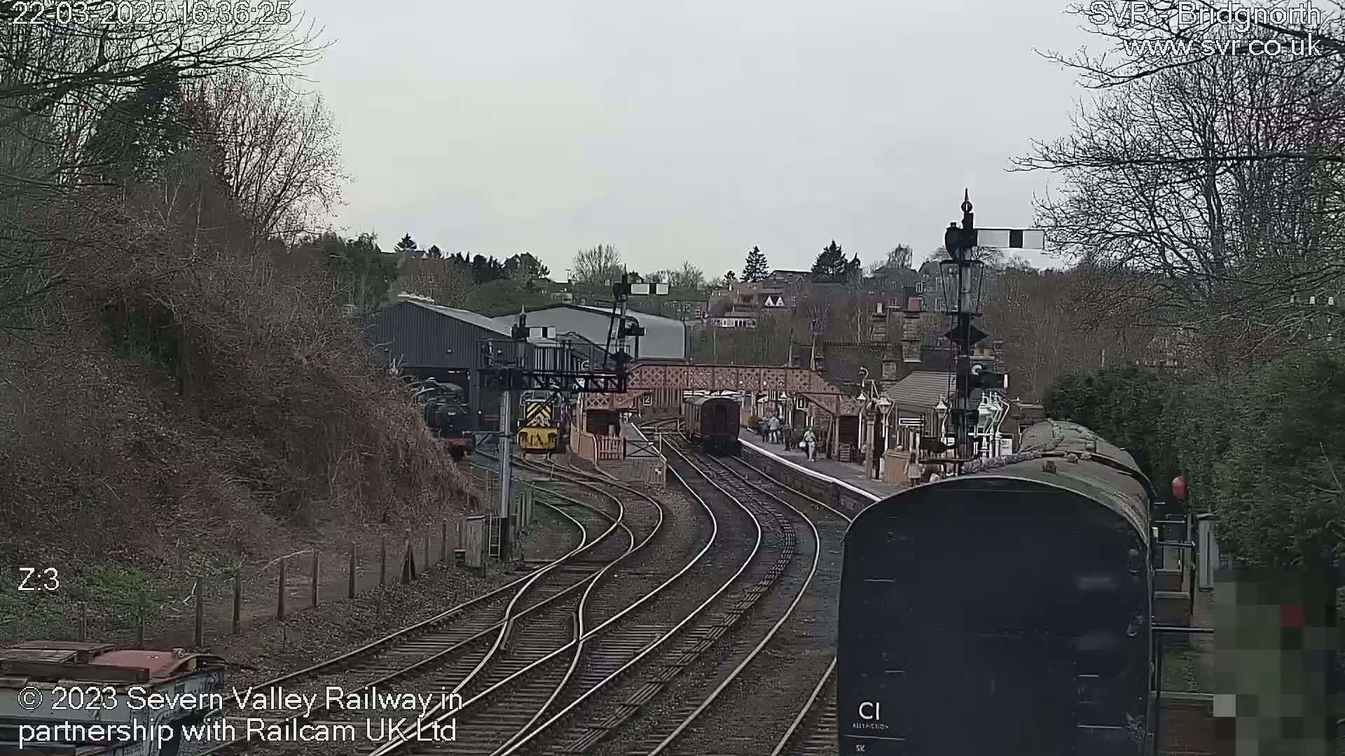 A train is departing from a railway station on an overcast day, with several tracks curving away from the viewer.