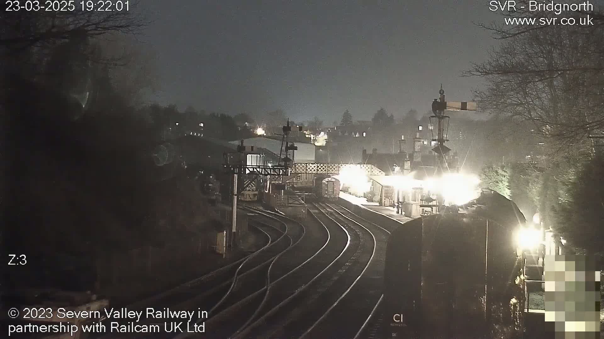 A nighttime view of a train station with several train cars on multiple tracks under hazy or foggy conditions.
