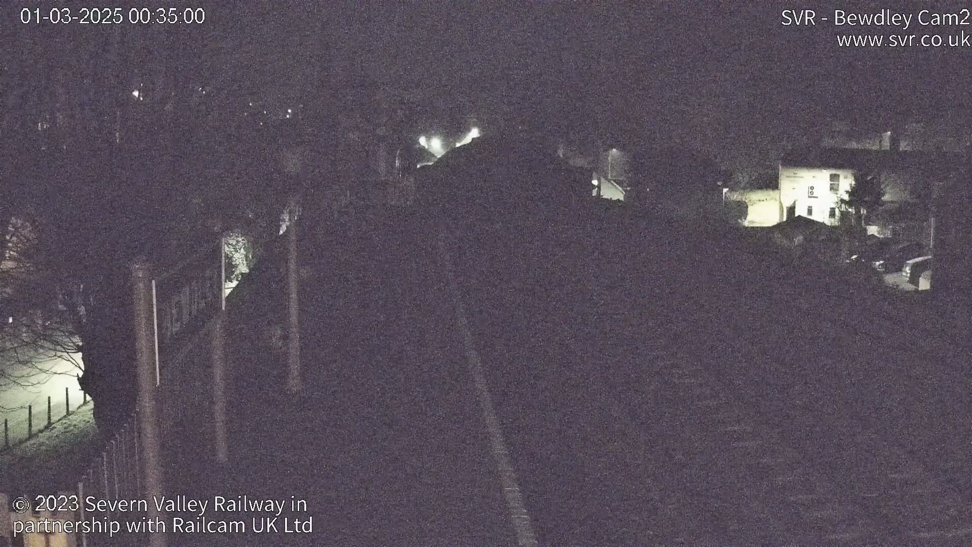 A nighttime, low-light view of a railway line and surrounding buildings under a dark sky.