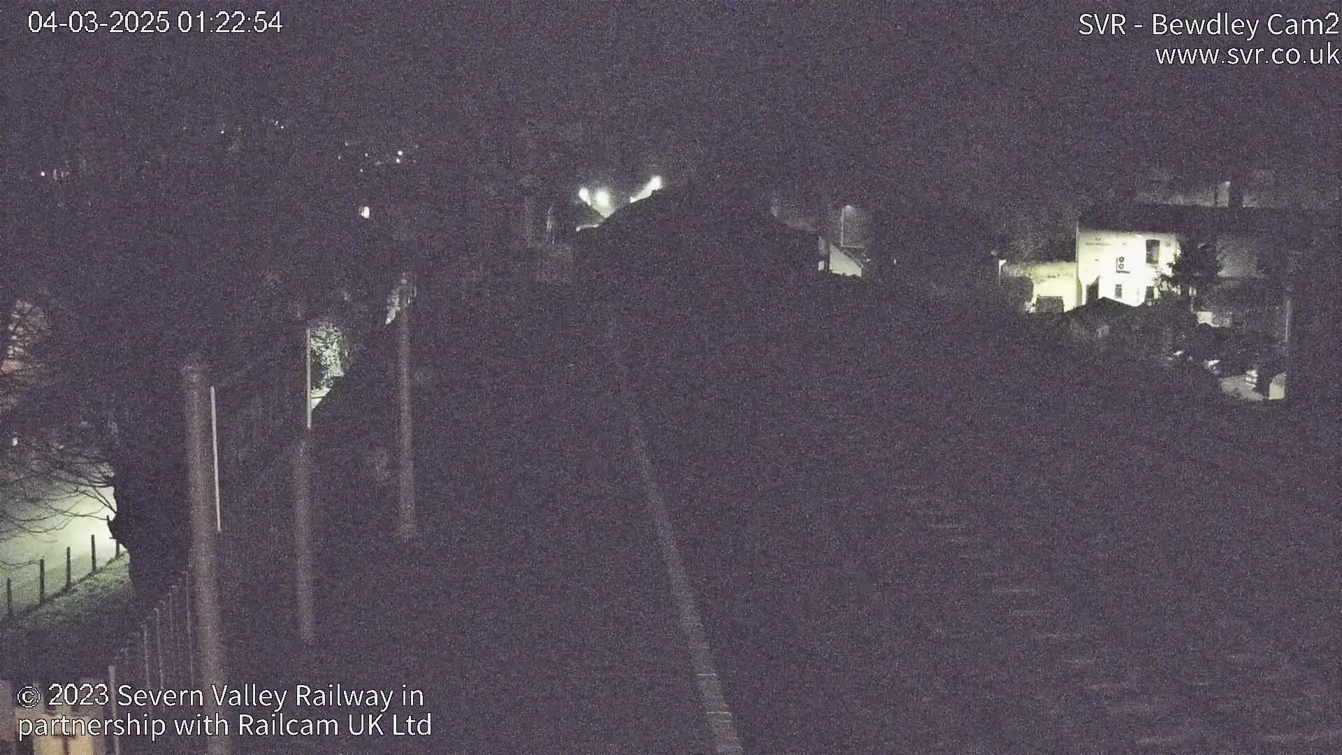 A nighttime, foggy view of a train track leading toward dimly lit buildings.