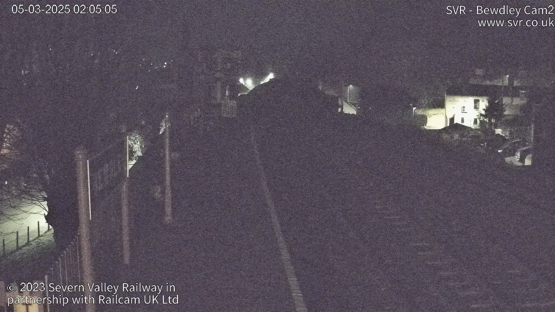 A nighttime, foggy view of a road leading towards buildings and trees.