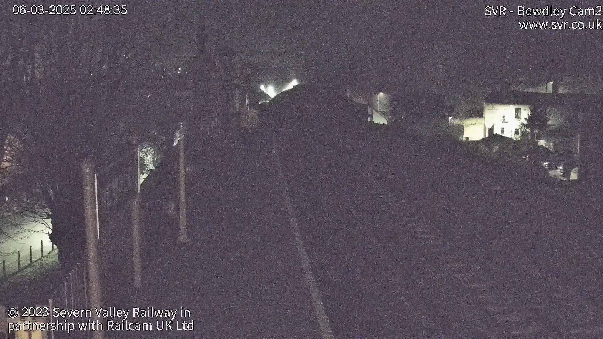 A nighttime, low-light view of a railway line leading to some dimly lit buildings.