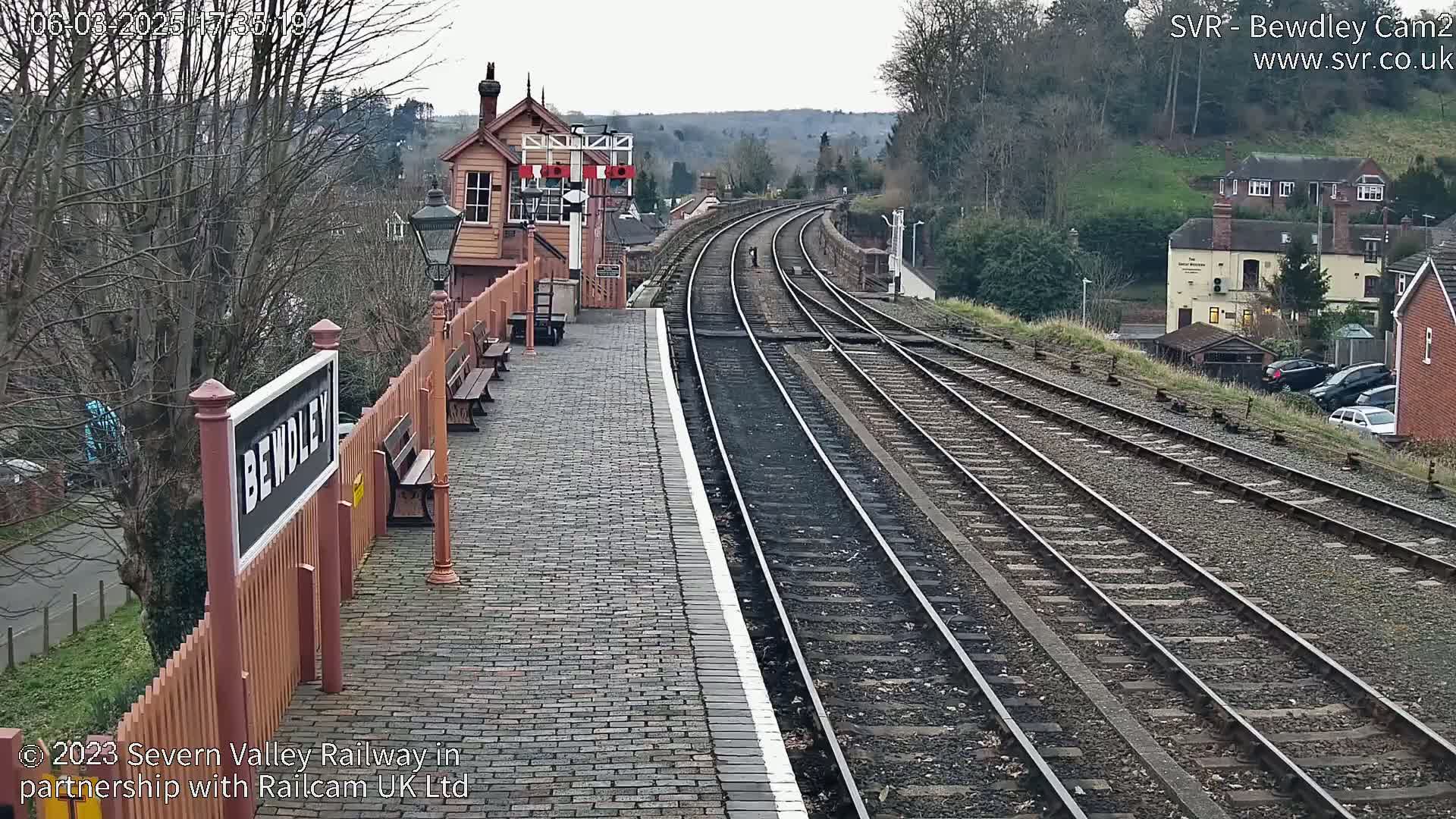 A brick train platform at Bewdley station, with multiple train tracks curving into the distance under an overcast sky.