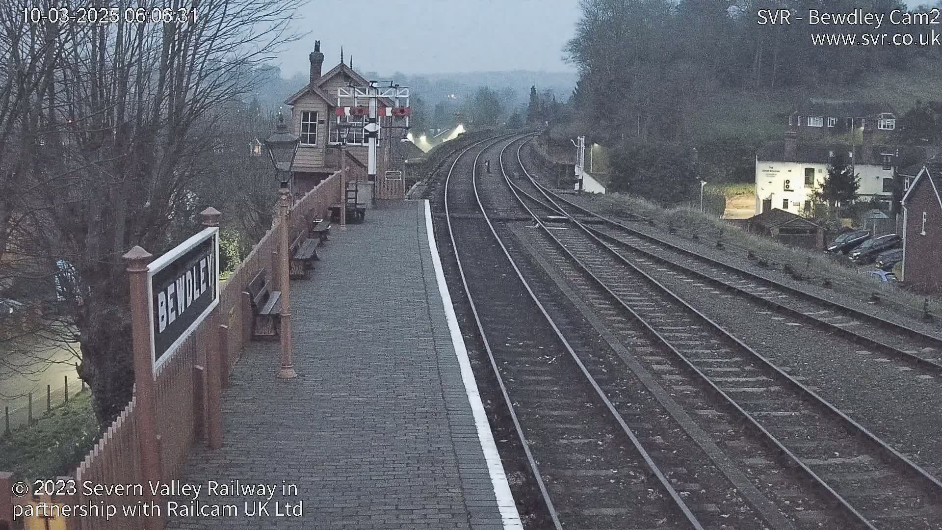 A train station platform with several tracks extending into the distance on a cloudy morning.