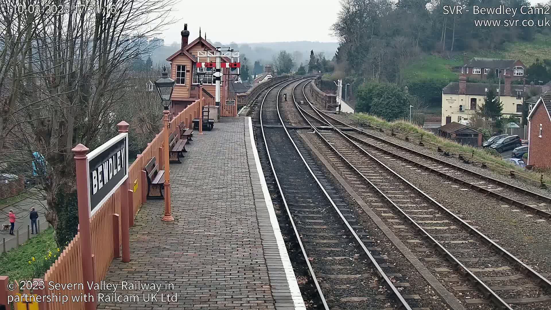 A train station platform with several train tracks curving into the distance on an overcast day.