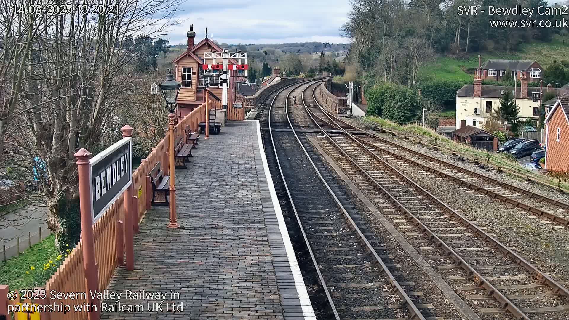 A brick train platform with a wooden signal box and two sets of railway tracks extending into the distance on an overcast day.