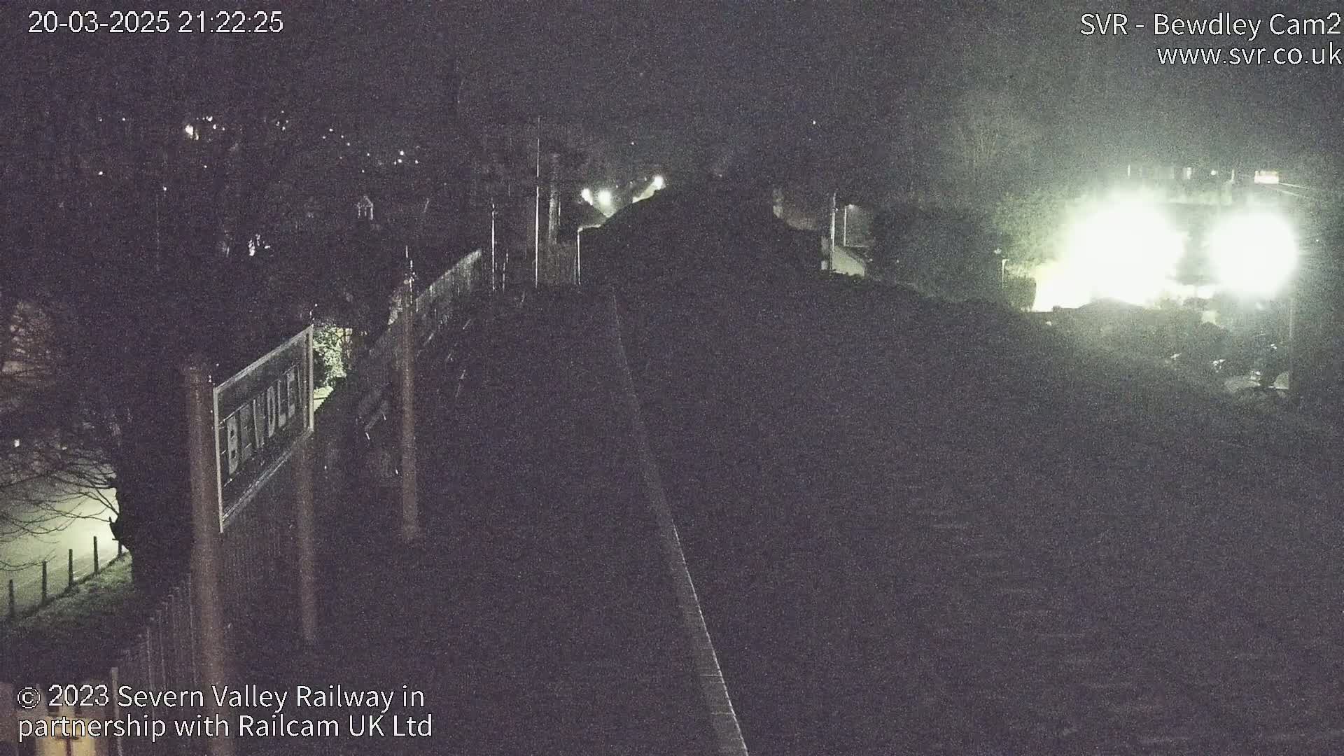 A nighttime, foggy view of a railway line and station, illuminated by artificial lights.