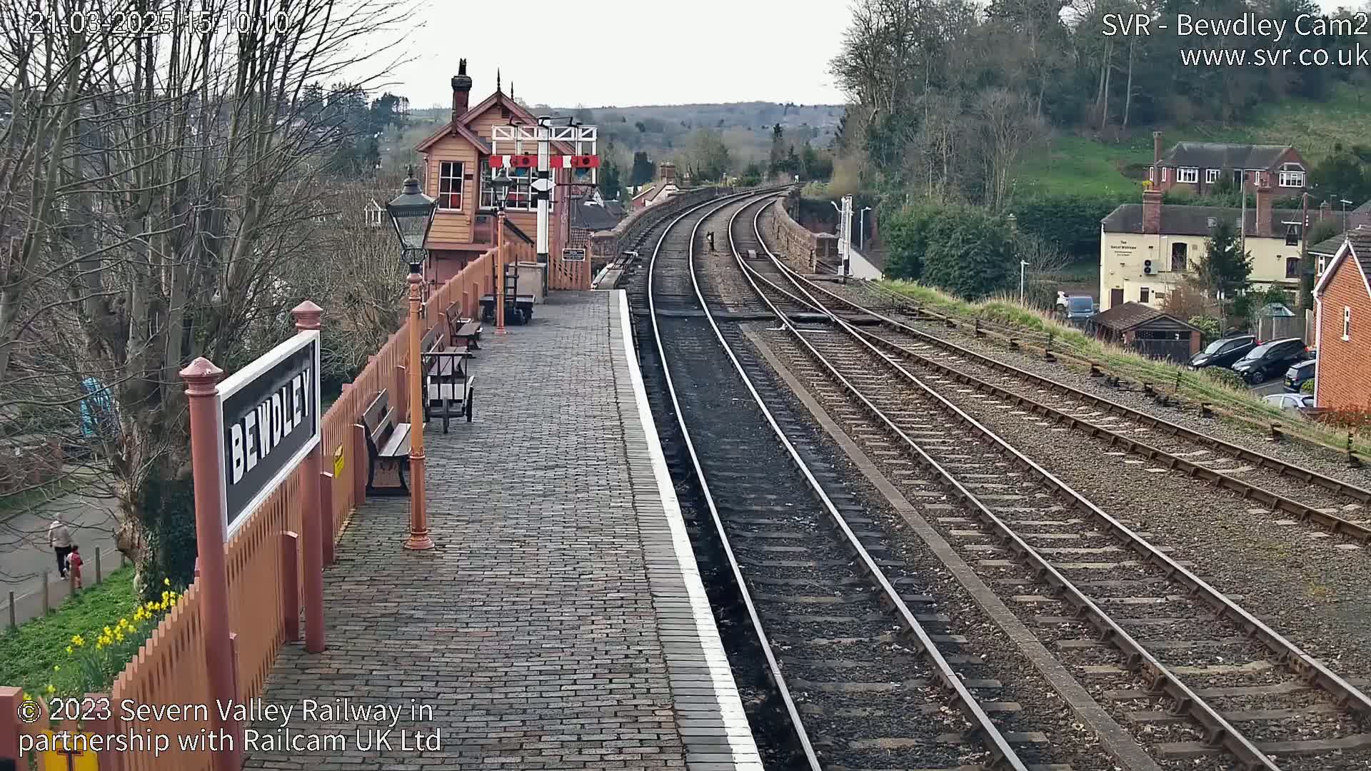 A brick train platform with a signal box and railway tracks extending into the distance under an overcast sky.