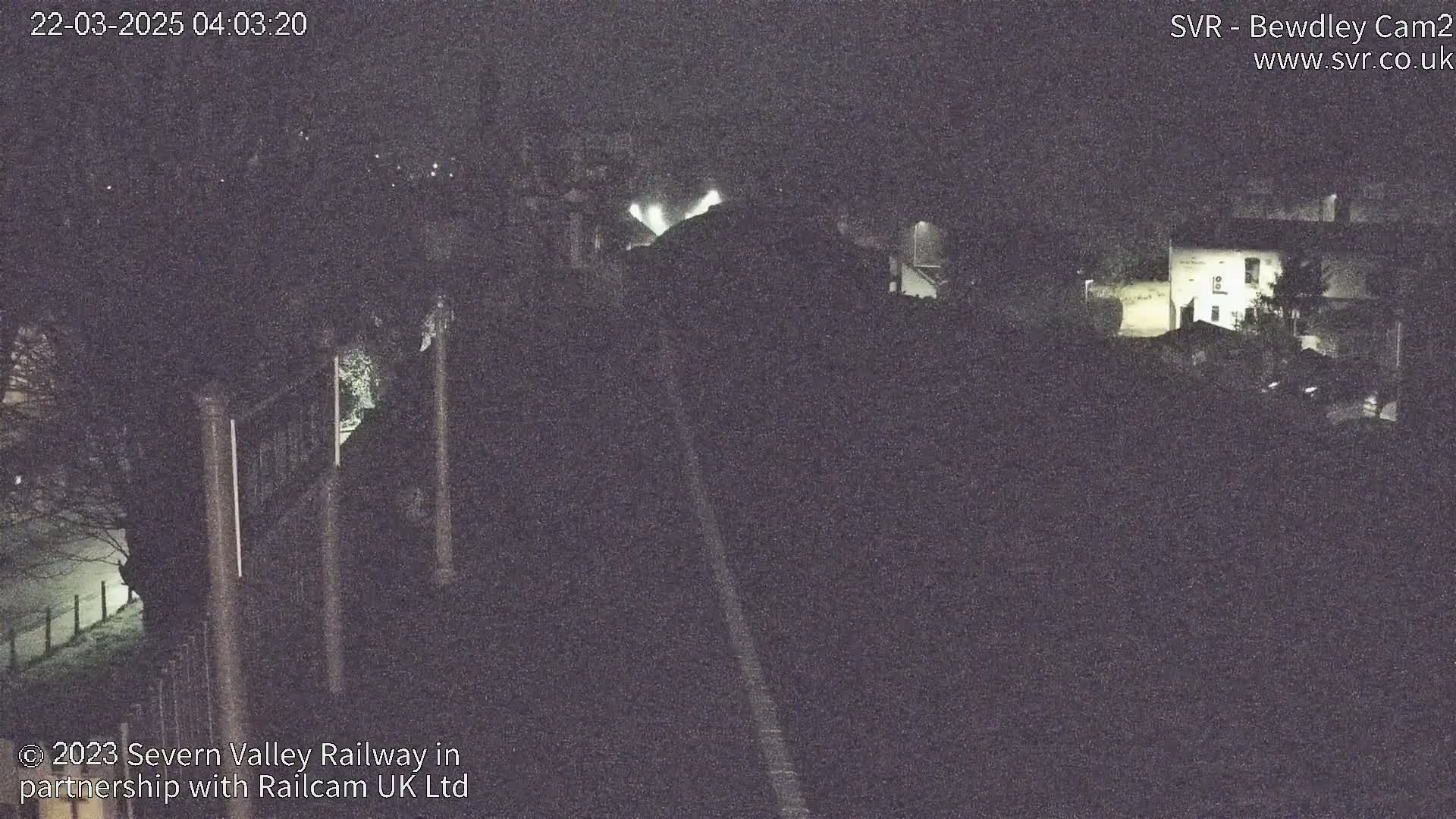 A nighttime, low-light view of a railway line and surrounding buildings under a dark sky.