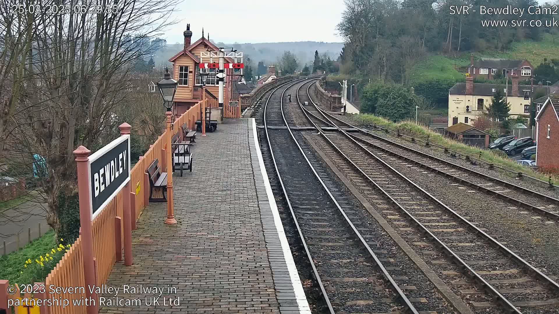 A train station platform with multiple train tracks extending into the distance on an overcast day.