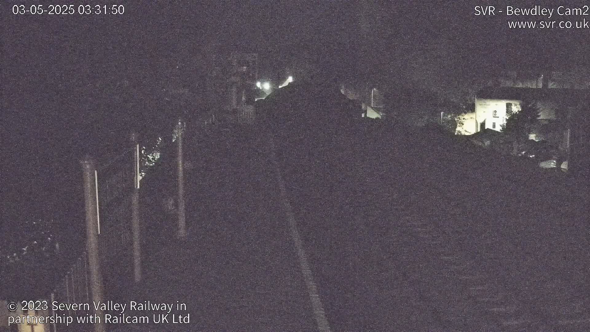 A nighttime view of a railway track and surrounding dark buildings under a dark sky.