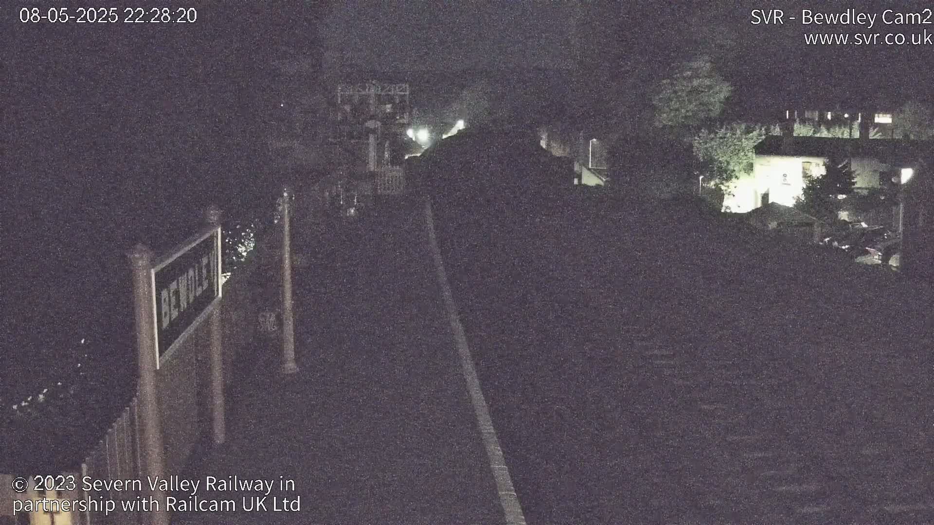 A nighttime view of a railway track and station sign, under a dark sky.