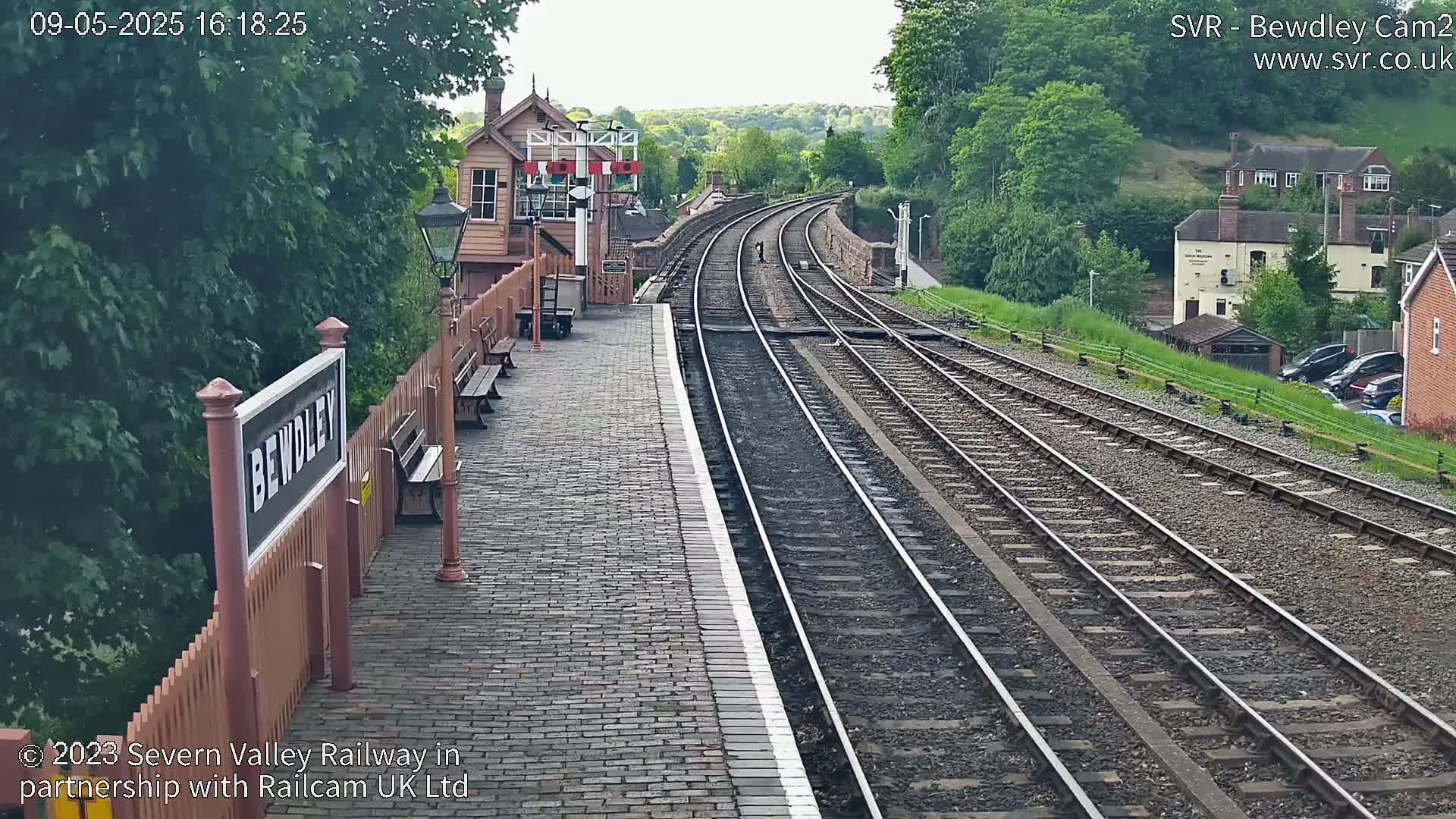 A brick railway platform with a signal box and multiple train tracks extending into the distance under a partly cloudy sky.