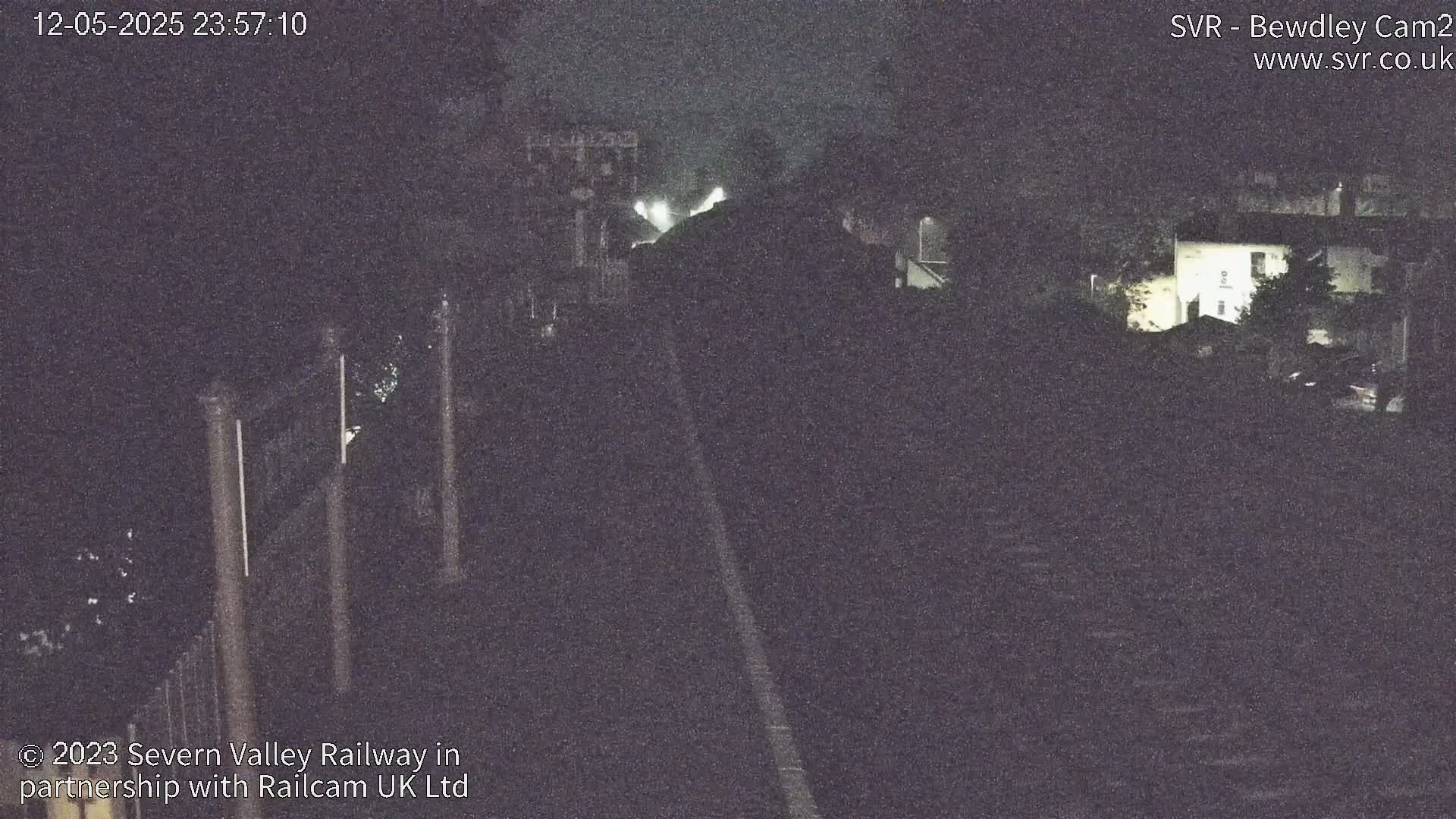 A nighttime, low-light view of a railway track and surrounding buildings under a dark sky.