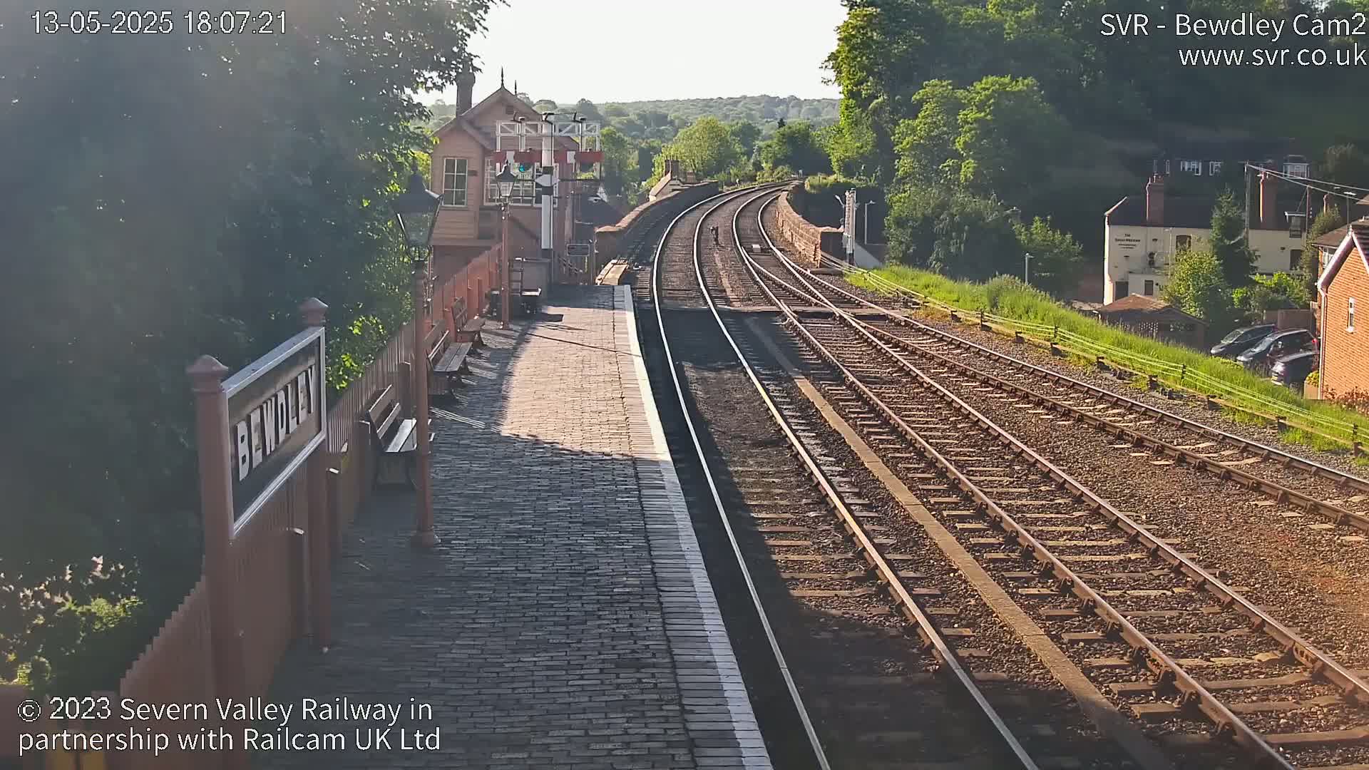 A sunny view of a railway station platform with multiple train tracks extending into the distance.