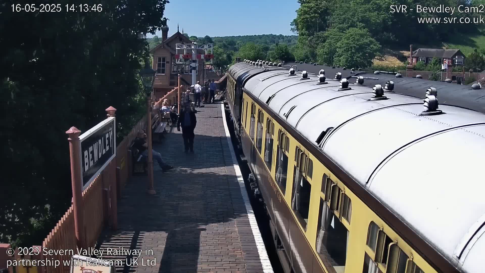 A long passenger train is at a station platform on a sunny day.
