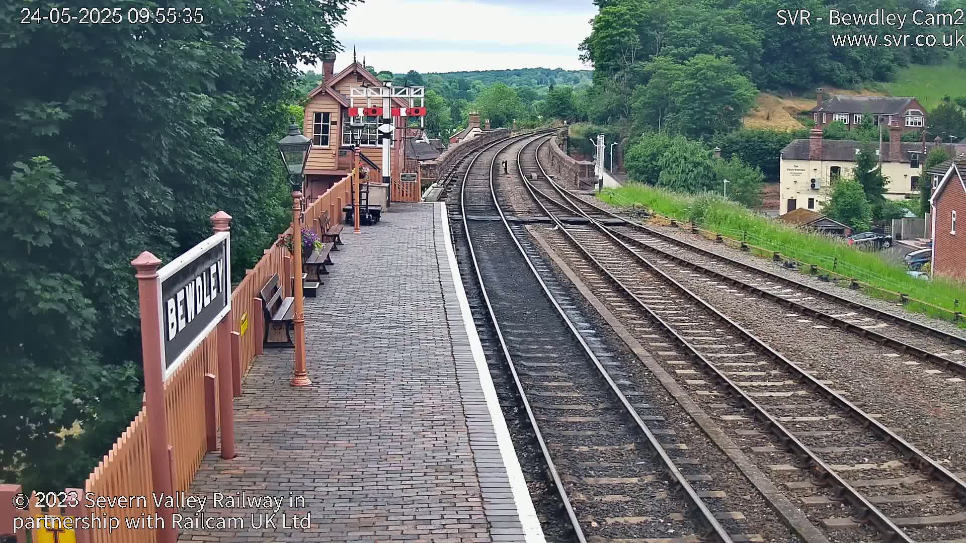 A brick railway platform with a signal box and multiple train tracks curving into the distance on an overcast day.
