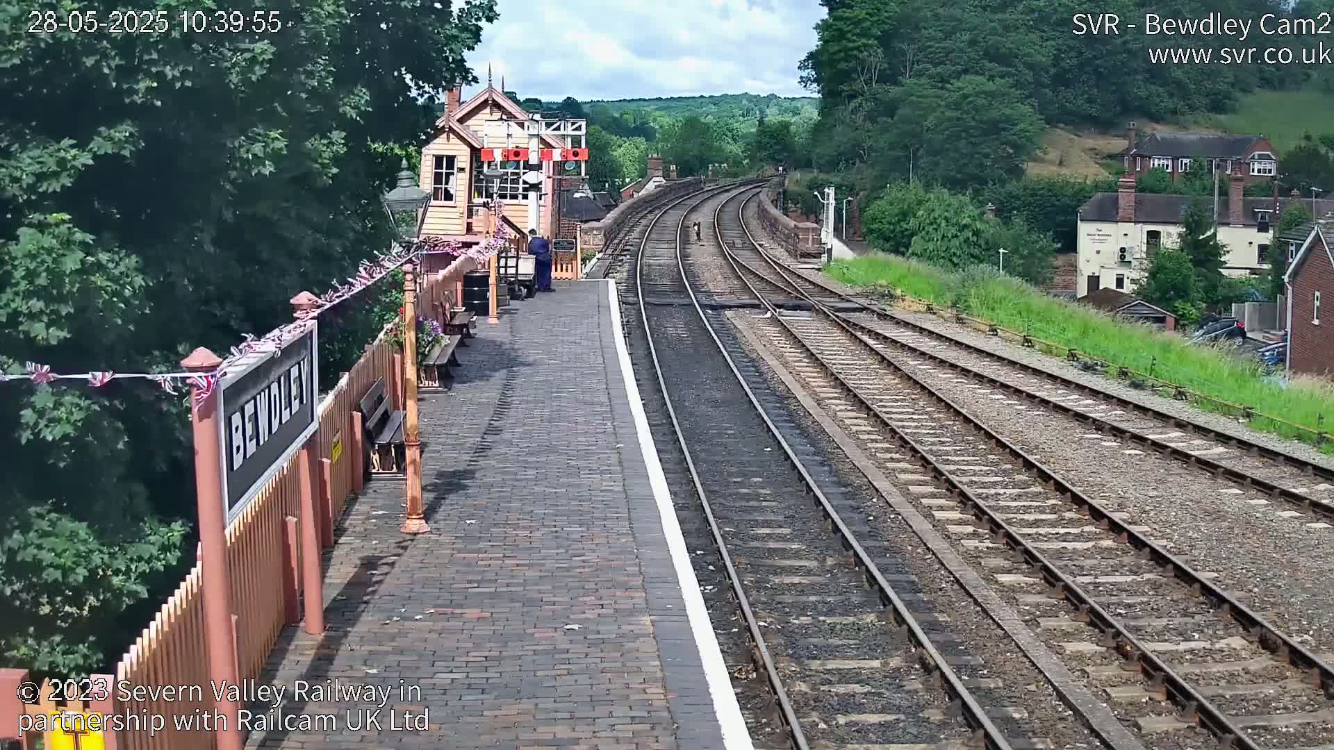 A train station platform with multiple train tracks curving into the distance under a sunny sky.