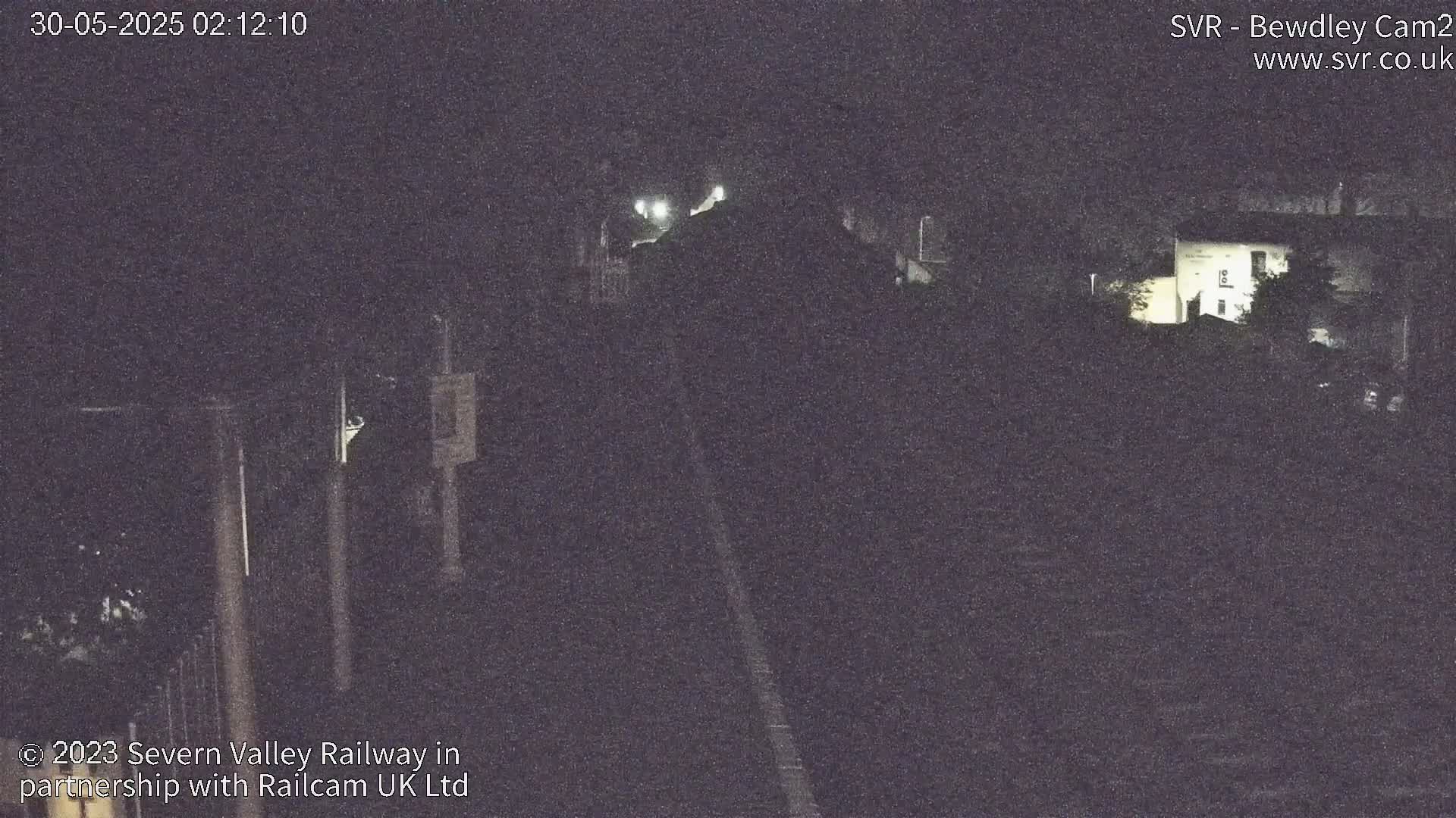 A nighttime, low-light view of train tracks and a building partially obscured by trees and darkness.