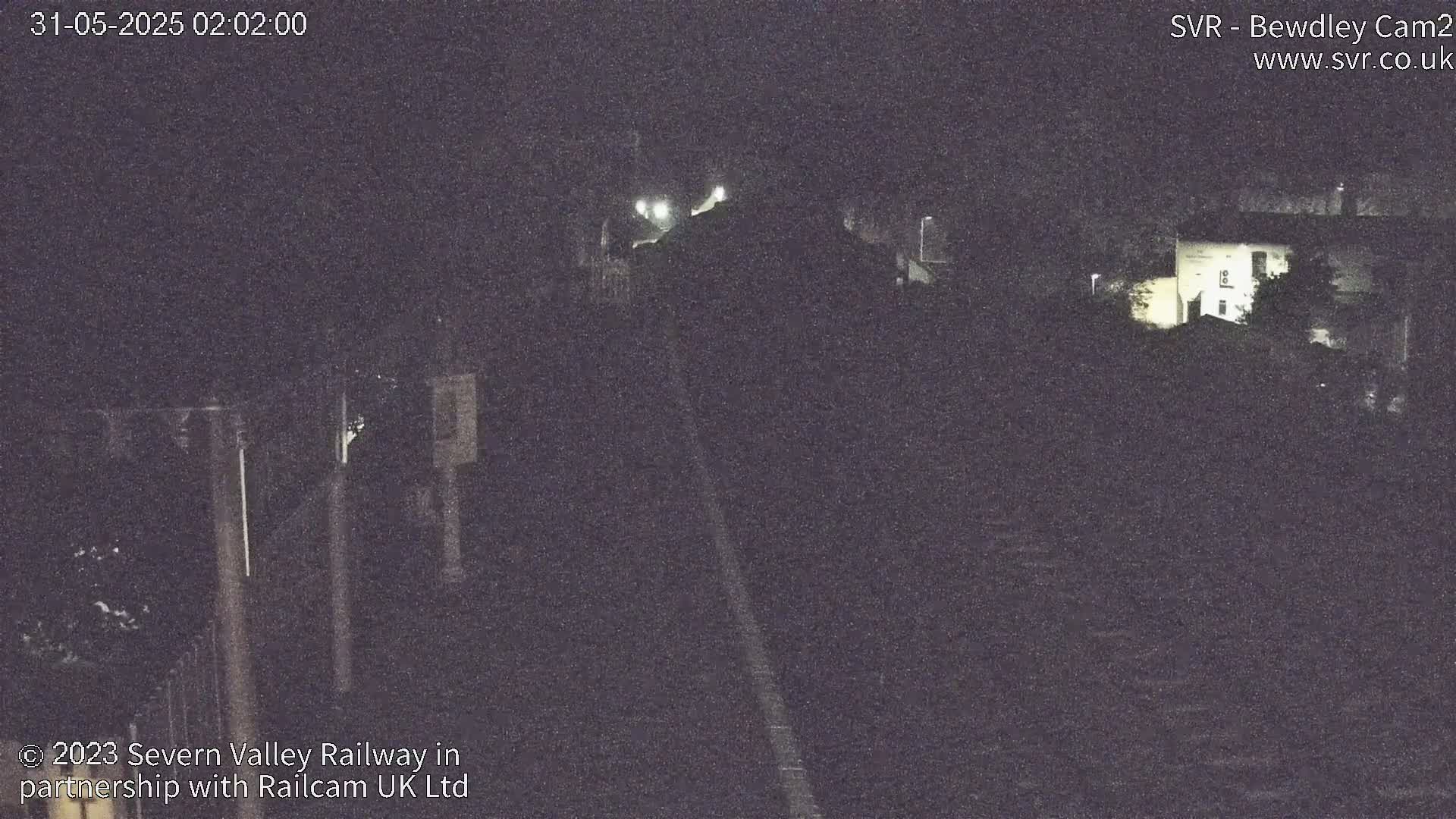 A nighttime, low-light view of a railway track leading to a building and trees.