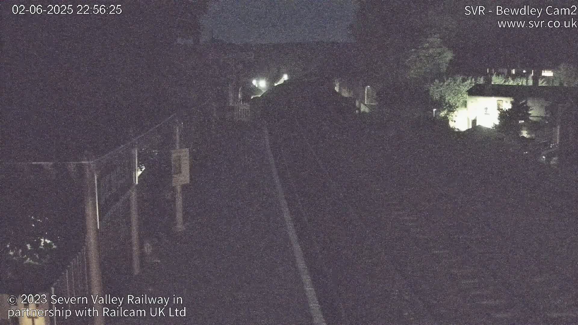 A nighttime, low-light view of a railway line leading towards a building partially obscured by trees.