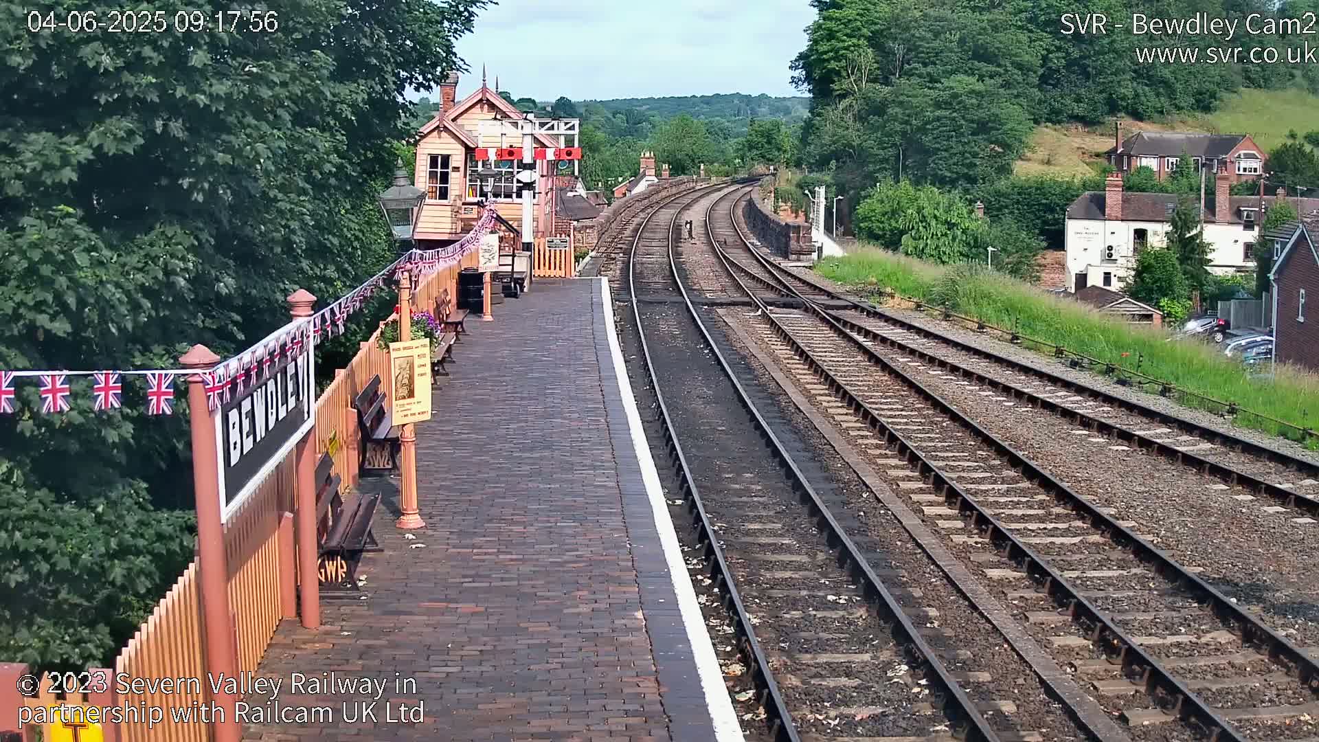 A brick railway platform with a signal box and multiple train tracks extending into the distance on a sunny day.