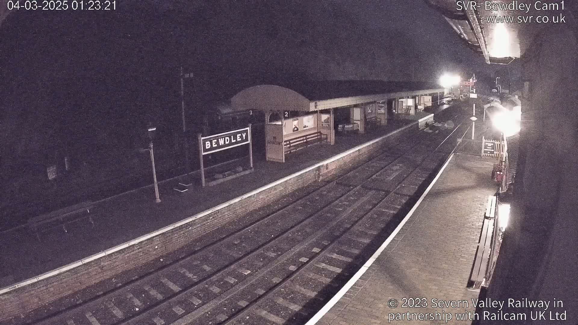 A nighttime view of a train station platform with train tracks extending into the darkness.
