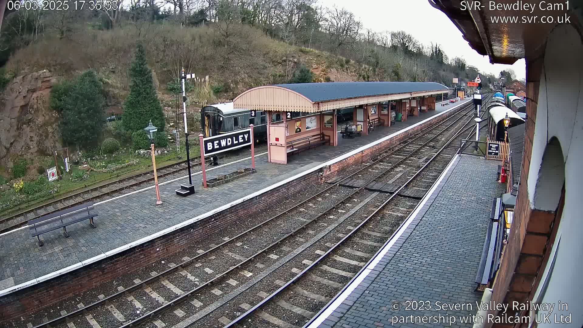 A train sits at a station platform next to a covered waiting area on an overcast day.