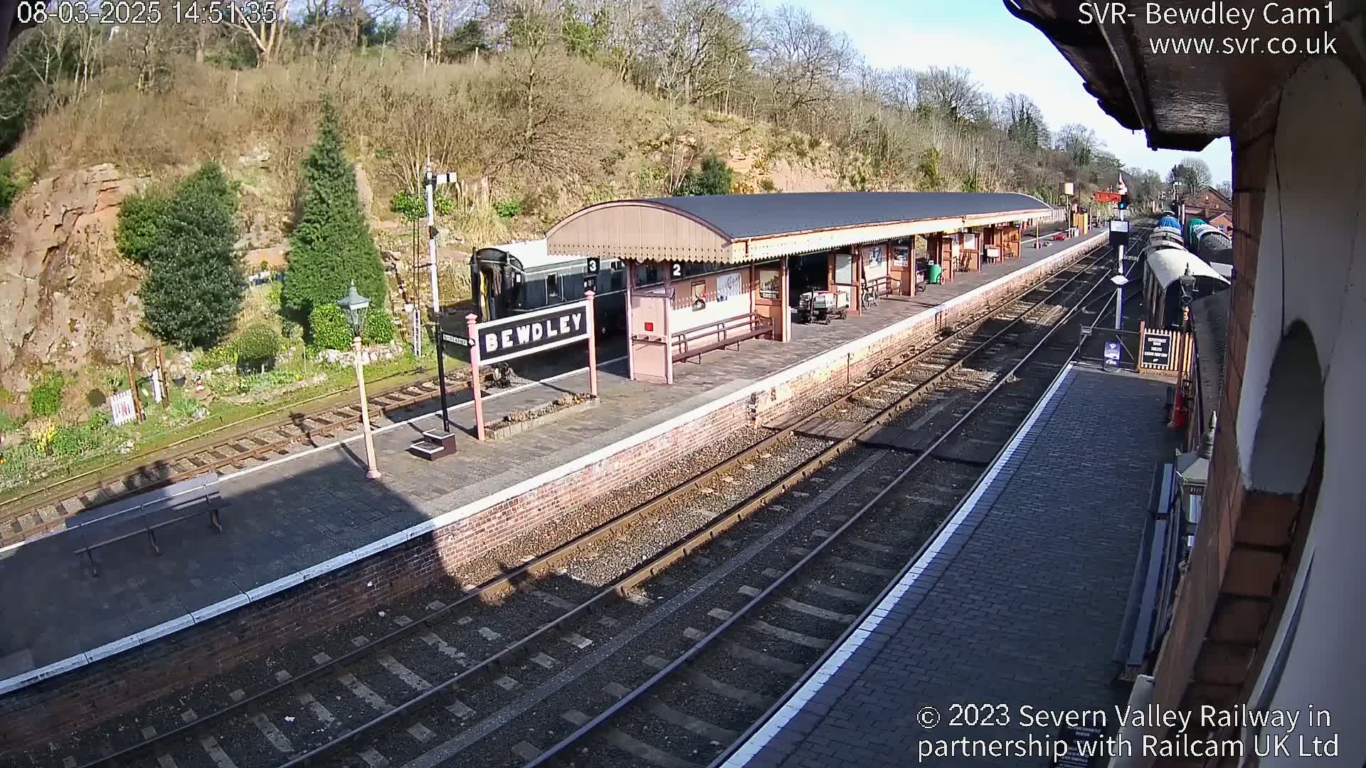 A train is stopped at a railway station platform on a sunny day.