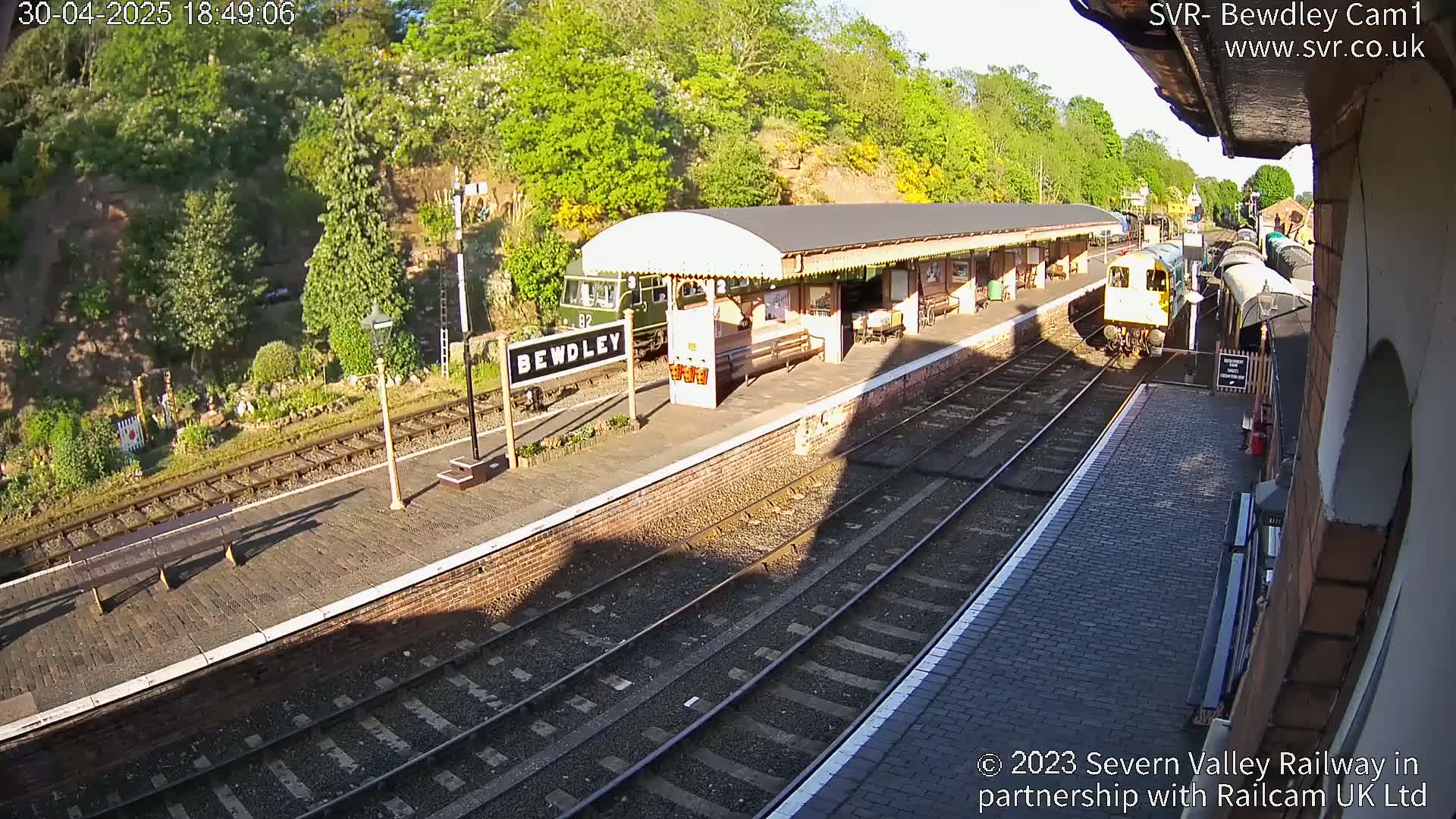A train is stopped at a railway station platform on a sunny afternoon.
