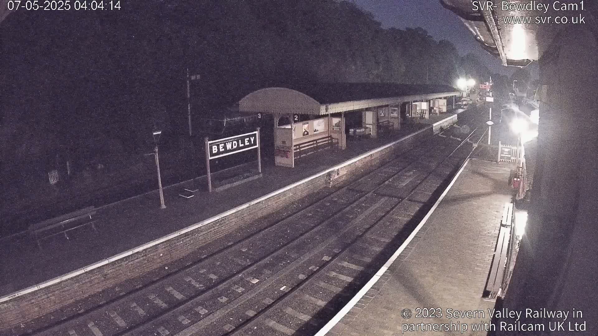 A nighttime view of a train station platform with multiple tracks and a partially visible station building.