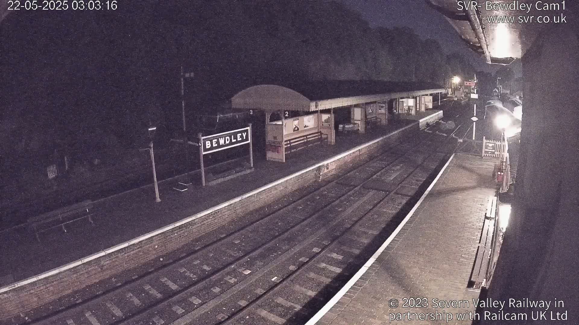 A nighttime view of a deserted train station platform with train tracks extending into the darkness.